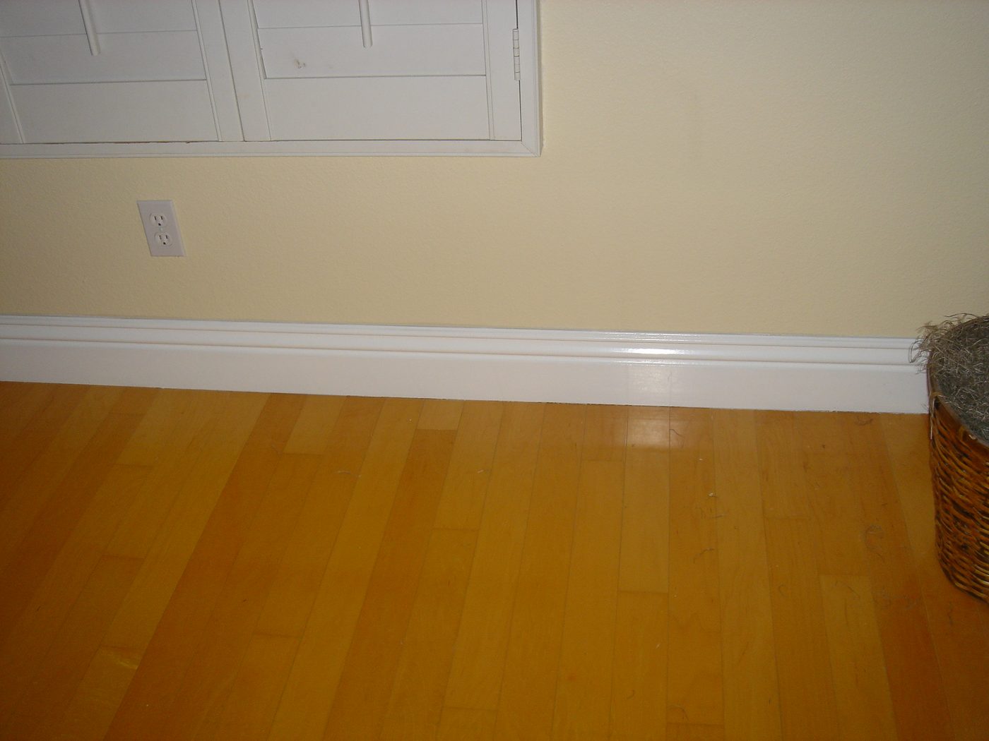 Freshly painted white baseboard trim along hardwood flooring in a bedroom